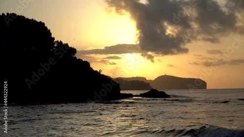 Sunrise on the coast, with the calm sea and the silhouette of a man on a hill taking photos. photo