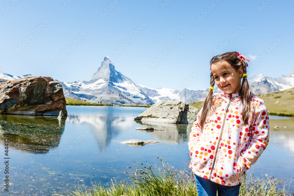 Naklejka premium Cute little girl outdoors in the lawn and admiring mountains view in mountain in switzerland