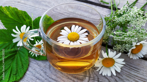 Chamomile tea. Flowers  leaves and a cup with tea on a wooden background. Drink with chamomile flowers.