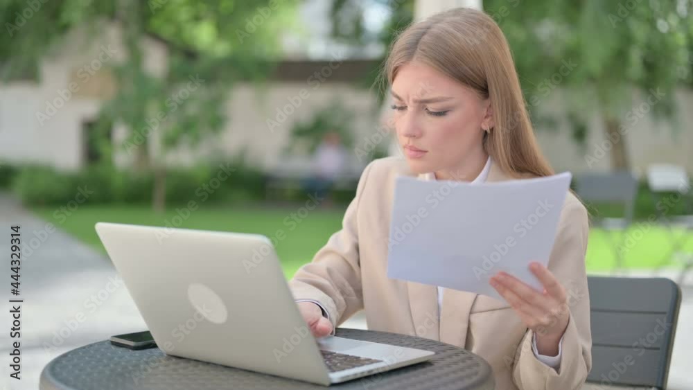 Young Businesswoman with Laptop Reading Documents in Outdoor Cafe Young Businesswoman with Laptop Reading Documents in Outdoor Cafe
