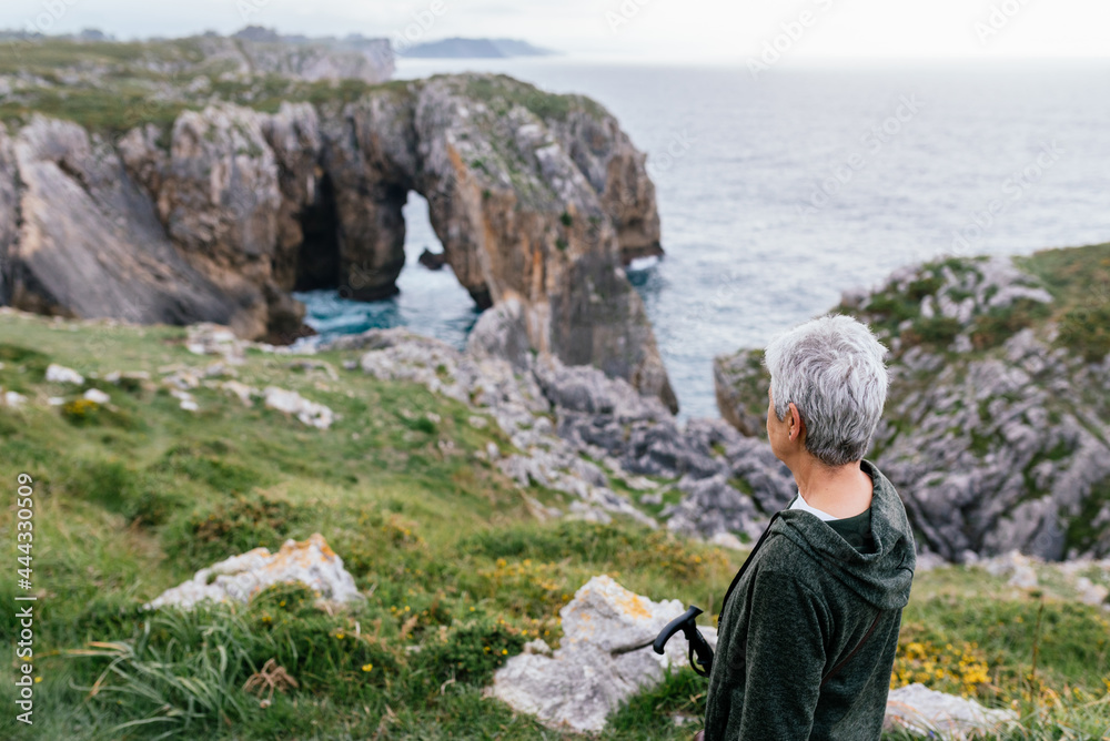 Older woman with short gray hair in front of sea cliffs in Ribadesella, Asturias, during a walk. old age and be fit.