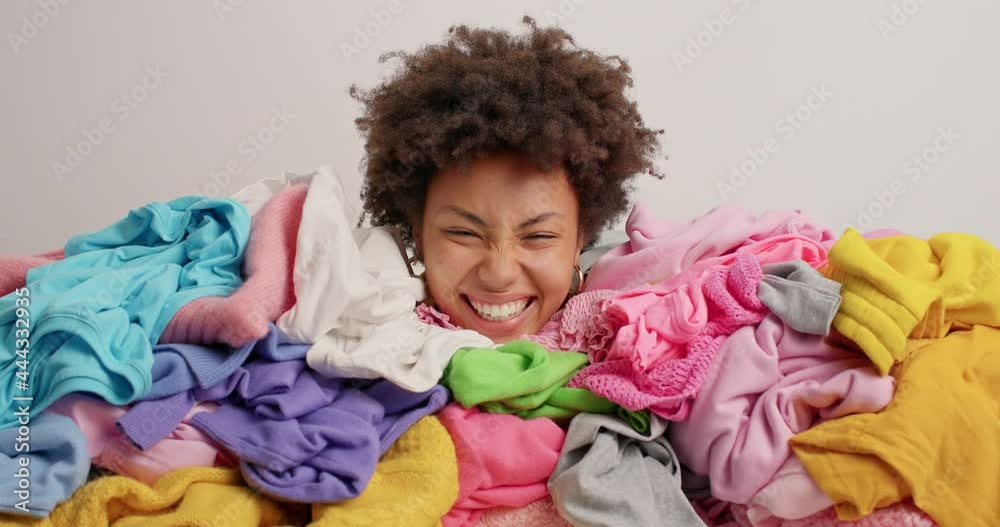 custom made wallpaper toronto digitalCurly haired woman buried in heap of laundry sorts out clothes in wardrobe has real chaos at home poses against white background. Afro American female covered with clothing stack for donation