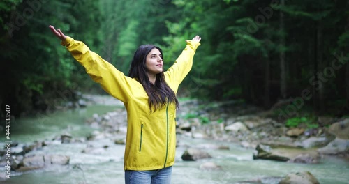 Beautiful young woman practicing relaxation tecniques, standing with arms spread and closed eyes amid forest in rainy weather, enjoying healing power of wild nature. photo