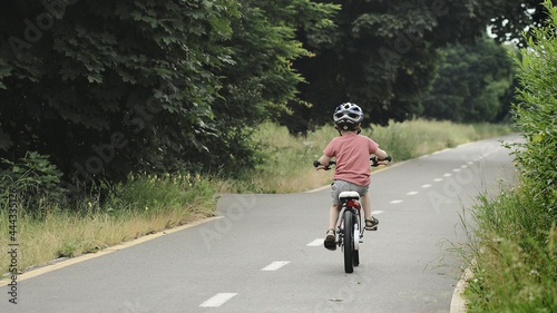 Fototapeta Naklejka Na Ścianę i Meble -  Child riding bicycle on the bike path at rain. Kid in helmet learning to ride at summer. Happy boy riding bike, having fun outdoors on nature.