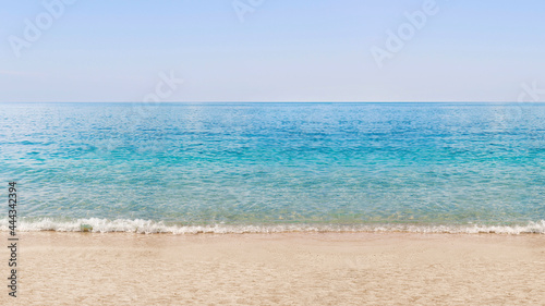A beach with white sand, turquoise ocean water and blue clear sky. Summer holidays. The concept of a tourist holiday on a summer beach on the island. View of an empty beach. Calm sea.