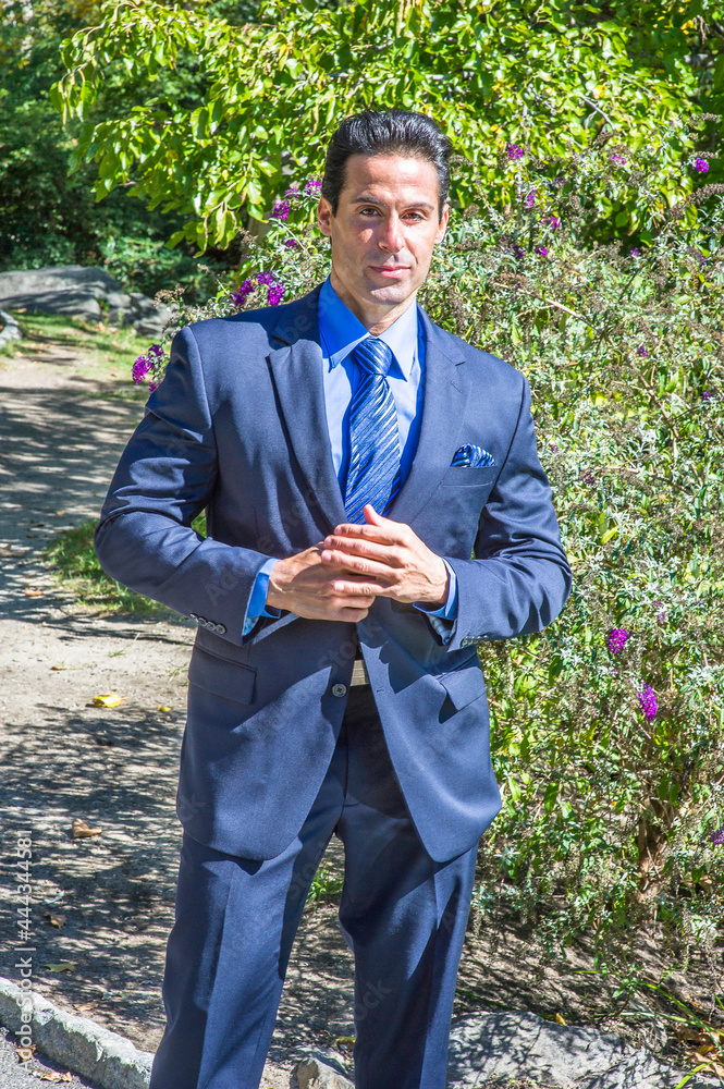 Dressing in a blue suit, blue shirt and blue pattern tie, a middle age handsome guy is standing outside and charmingly looking at you. . Dressing in a blue suit, blue shirt and blue pattern tie, a middle age handsome guy is standing outside and charmingly looking at you. .