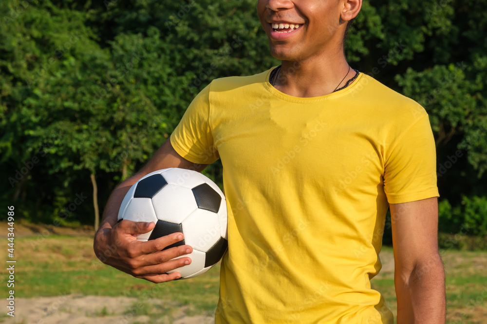 Happy African-American man holding soccer ball while standing outdoors in park