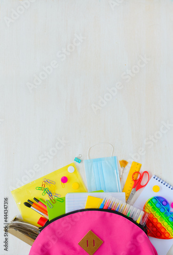 Back to school. Bright colorful school supplies in backpack for school or college on white wooden background. Stationery for school children's studies. Greeting card. layout. vertical