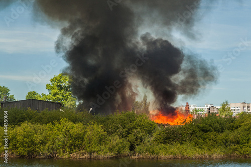 Burning bushes on the banks of the river. A sawmill fire and a huge plume of smoke