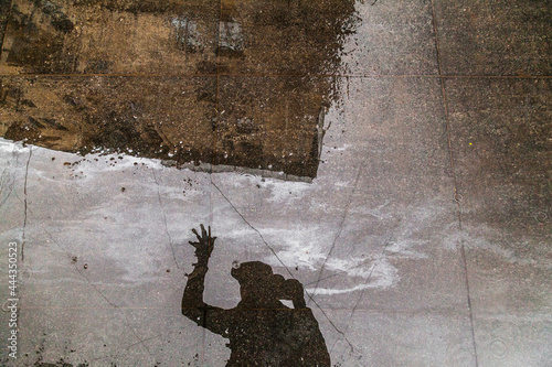 Reflection of man's silhouette and old house in a puddle on a granite slab with traces of gasoline stains