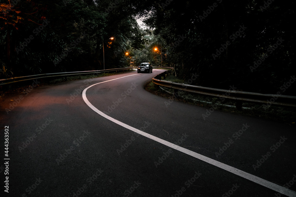 A less busy road with a moody environment having a car in motion A less busy road with a moody environment having a car in motion