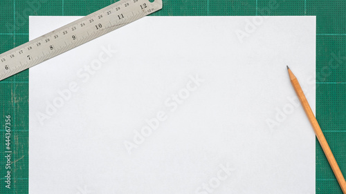 Top view of blank paper page A4 on old green cutting mat with stainless steel ruler, pencil, copy space for text, flat lay.