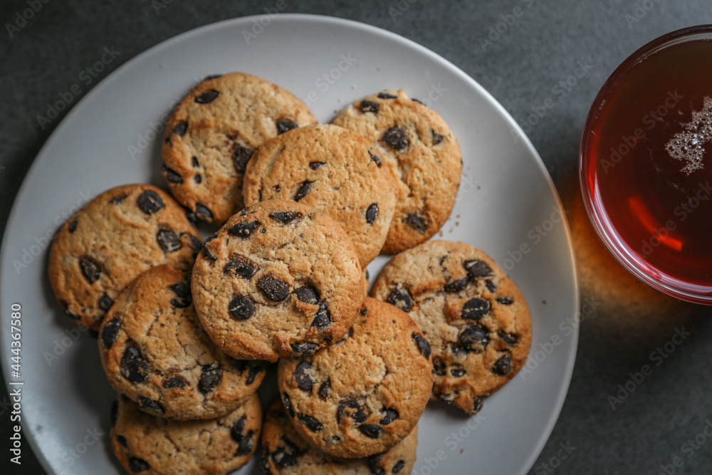 A cup of hot black tea in a glass cup and a gray ceramic plate with cookies with chocolate chips on a gray ceramic tabletop