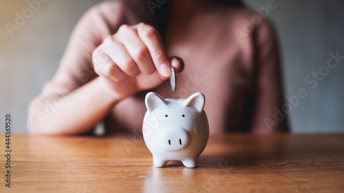 Closeup image of a woman putting coins into piggy bank for saving money concept