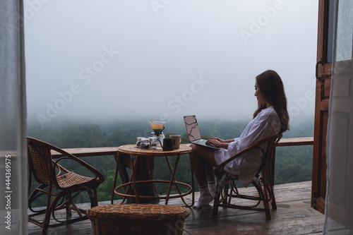 A woman using and working on laptop computer while sitting on balcony with a beautiful nature view on foggy day