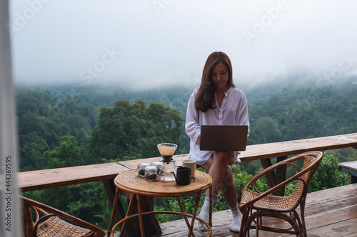 A woman using and working on laptop computer while sitting on balcony with a beautiful nature view on foggy day
