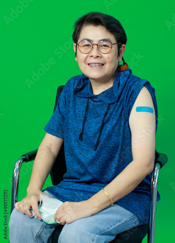 Adult senior Asian woman sitting confident show shoulder with bandage plaster after getting Coronavirus of Covid-19 vaccine injection. Idea for vaccination of population against virus.
