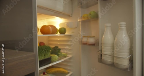 Unsurpassed brunette girl wearing a white T-shirt against the background of the kitchen comes to the fridge, surprisedly opens it, chooses a cheesecake on a white plate, enjoying the smell of it. photo