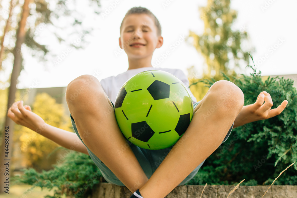 Teenager in white t-shirt holding green soccer ball meditating about good football, soccer game result. Green background, nature
