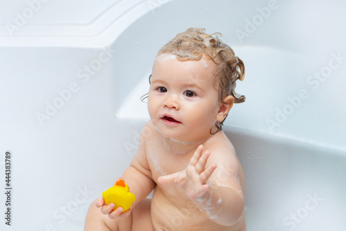 Lovely child playing with foam. Happy baby taking a bath playing with foam bubbles. Little child in a bathtub. Smiling kid in bathroom with toy duck. Infant washing and bathing. Kids care and hygiene.