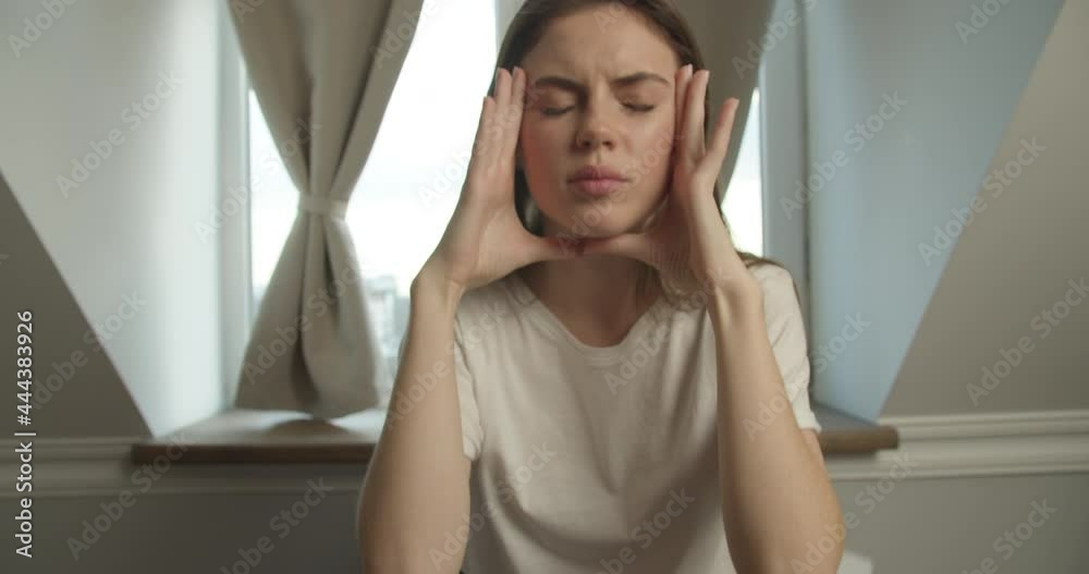 Beautiful girl brunette of Slavic appearance sits in a white T-shirt at the desk, scatters sheets of paper and upsetly presses his hands to the temples, looking away against Beautiful girl brunette of Slavic appearance sits in a white T-shirt at the desk, scatters sheets of paper and upsetly presses his hands to the temples, looking away against