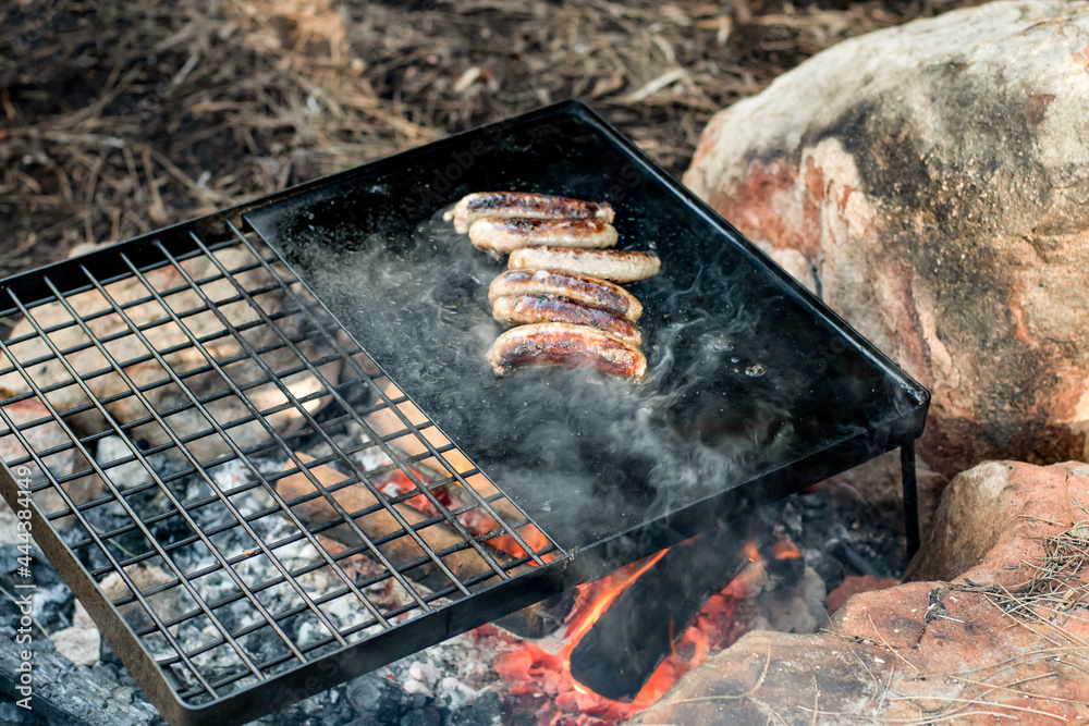 Camp cooking. Grilling sausages on a cast iron plate over the camp fire. Camp cooking. Grilling sausages on a cast iron plate over the camp fire.