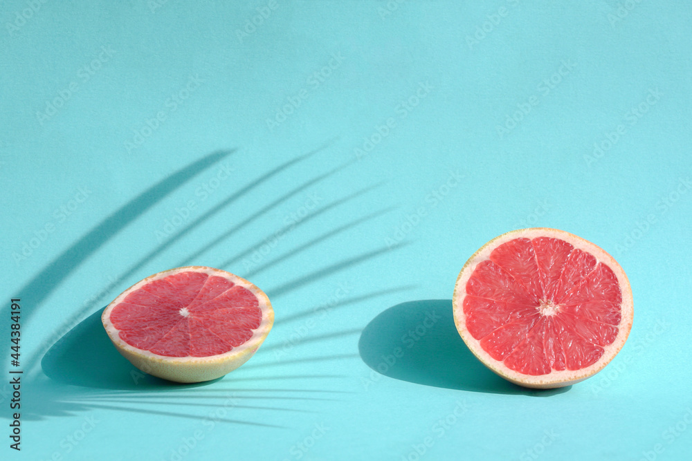 Summer still life with two cut grapefruits with palm leaves harsh shadows. On blue background. Summer still life with two cut grapefruits with palm leaves harsh shadows. On blue background.