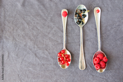 Red and black currant and loganberries on the iron spoon on the gray background.