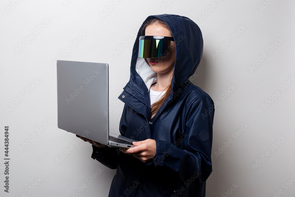 Young woman in virtual reality glasses holds a laptop on a light background