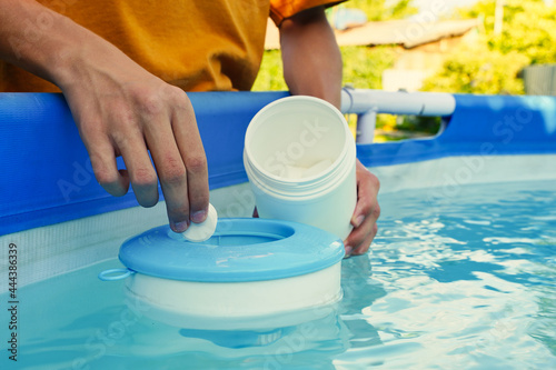 Hand holding white chlorine tablets over swimming pool skimmer. Chlorination of water in pool for disinfection and prevention against the development of microbes. photo