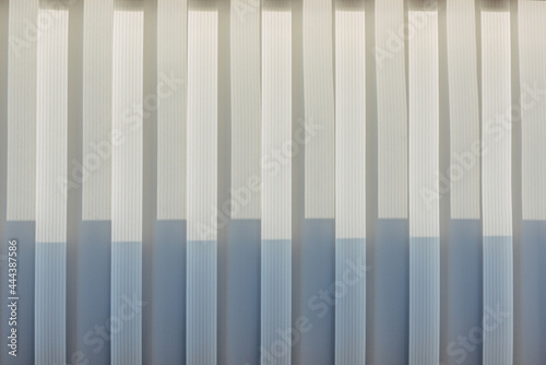 Abstract geometric vertical lines white and gray gradient color. Repeating pattern  background texture  design of striped lines. Blinds illuminated by the sun  close-up.