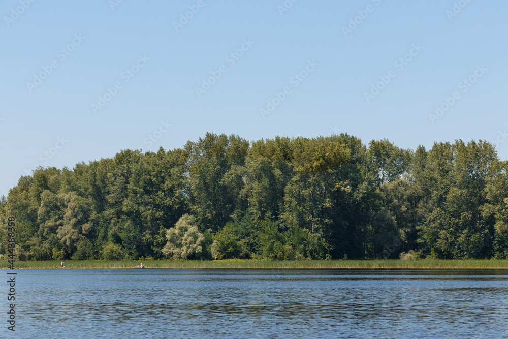 summer landscape with a river, floating people on boats in the distance, green beach, smooth water summer landscape with a river, floating people on boats in the distance, green beach, smooth water