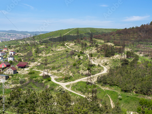 A power transmission line support with wires near a village on the green mountains of the Krasnodar Territory, Novorossiysk, Russia. Landscapes of rural, suburban areas.