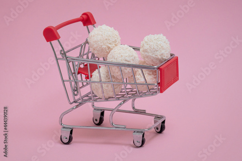 sweet coconut balls in supermarket trolley on pink background, sale, discount on desserts, online shopping photo