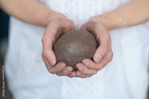 women's hands holding a grey ball. Prepare to work in a pottery workshop. Pottery made of clay with their own hands. photo