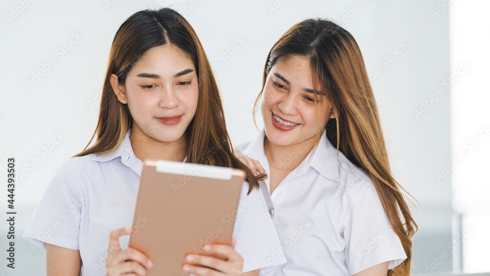 Asian sibling college students in student uniform interacting and looking at a digital tablet to study together on the university campus. Education stock photo Asian sibling college students in student uniform interacting and looking at a digital tablet to study together on the university campus. Education stock photo