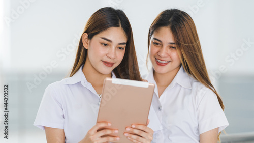 Asian sibling college students in student uniform interacting and looking at a digital tablet to study together on the university campus. Education stock photo