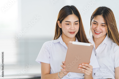 Asian sibling college students in student uniform interacting and looking at a digital tablet to study together on the university campus. Education stock photo