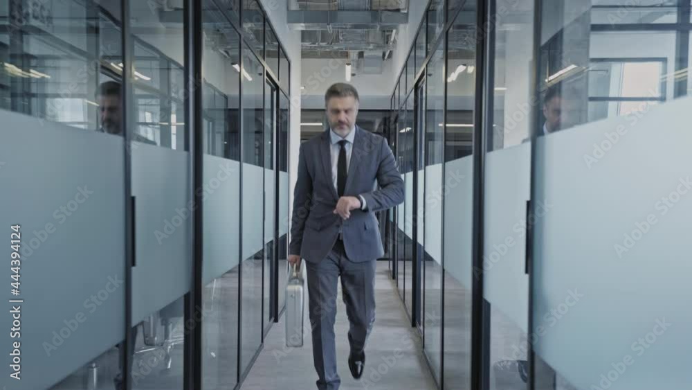Successful businessman walking office corridor, looking at watch before meeting Successful businessman walking office corridor, looking at watch before meeting