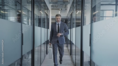 Successful businessman walking office corridor, looking at watch before meeting