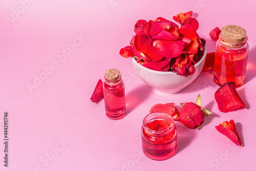 Bottles of essential oil and roses petals on pink background photo