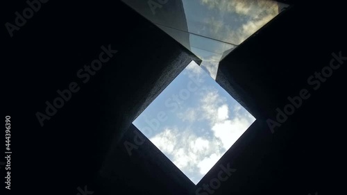 Low angle shot of camera rotating in square ceiling architecture detail. Blue sky background.
