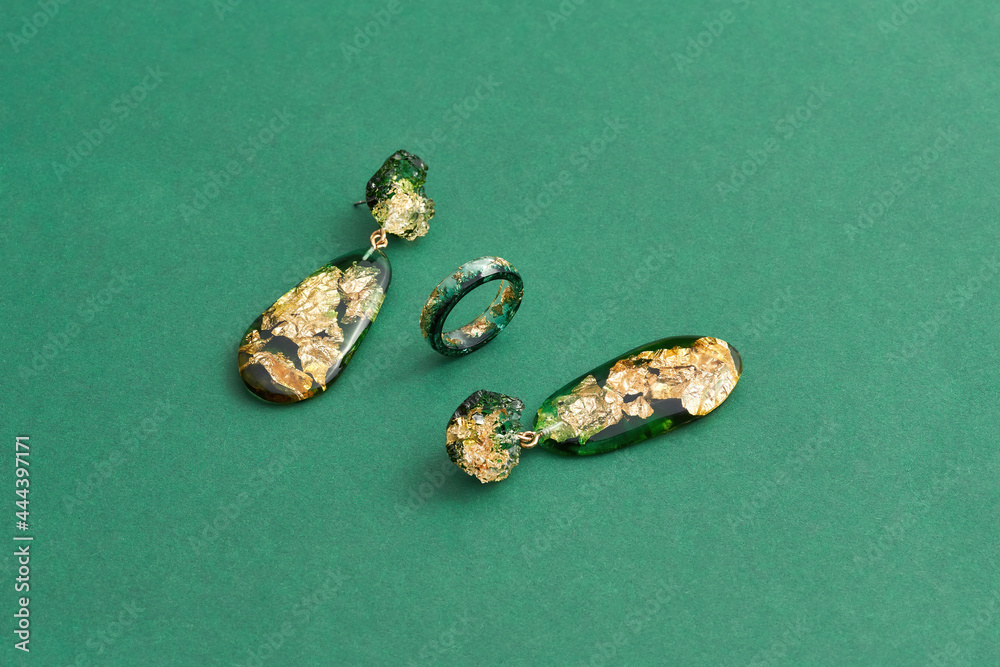 Set of a ring and dangle earrings made of epoxy resin with golden foil inside isolated over green background Set of a ring and dangle earrings made of epoxy resin with golden foil inside isolated over green background