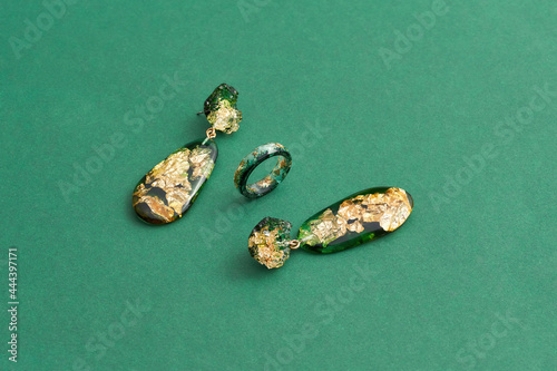 Set of a ring and dangle earrings made of epoxy resin with golden foil inside isolated over green background photo