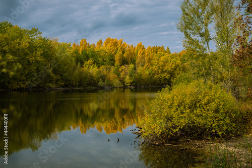Autumn landscape - forest lake. Lake with shores overgrown with trees with yellow autumn leaves, which are reflected in the water along with the sky with clouds