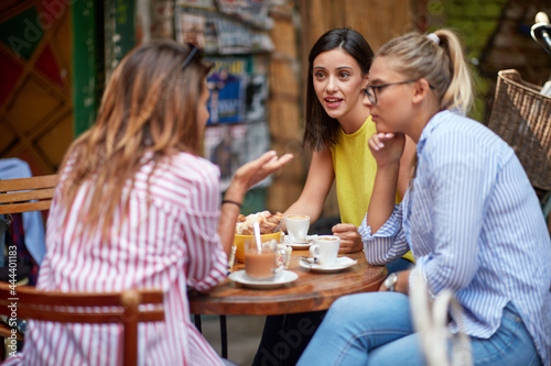 group of young adult caucasian female friends talking, sitting in outdoor cafe, drinking coffee.