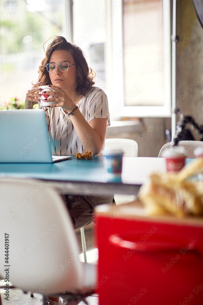 A young woman is enjoying a coffee while working in the office