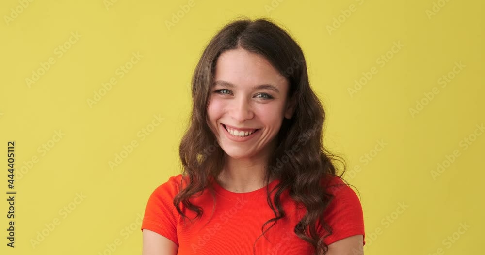 Smiling woman saying no by waving her finger over yellow background