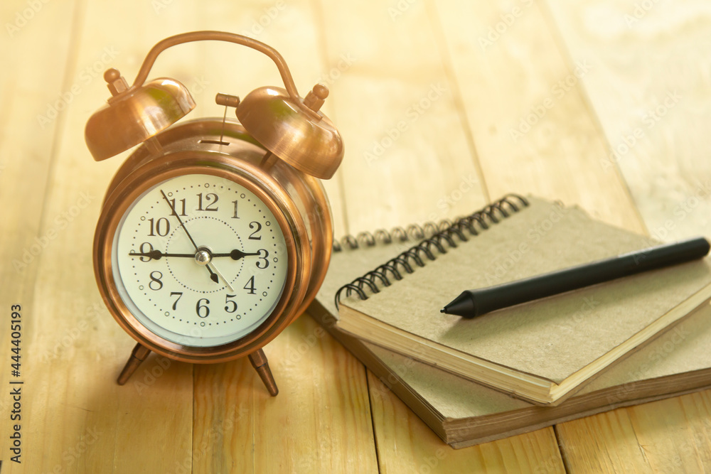 Golden alarm clock with note book on wooden table and golden light in the morning. Golden alarm clock with note book on wooden table and golden light in the morning.