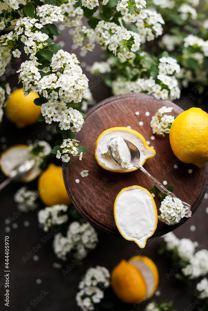 Lemon souffle in halves of lemons on a wooden stand among spirea flowers. Citrus dessert. Lemon souffle in halves of lemons on a wooden stand among spirea flowers. Citrus dessert.